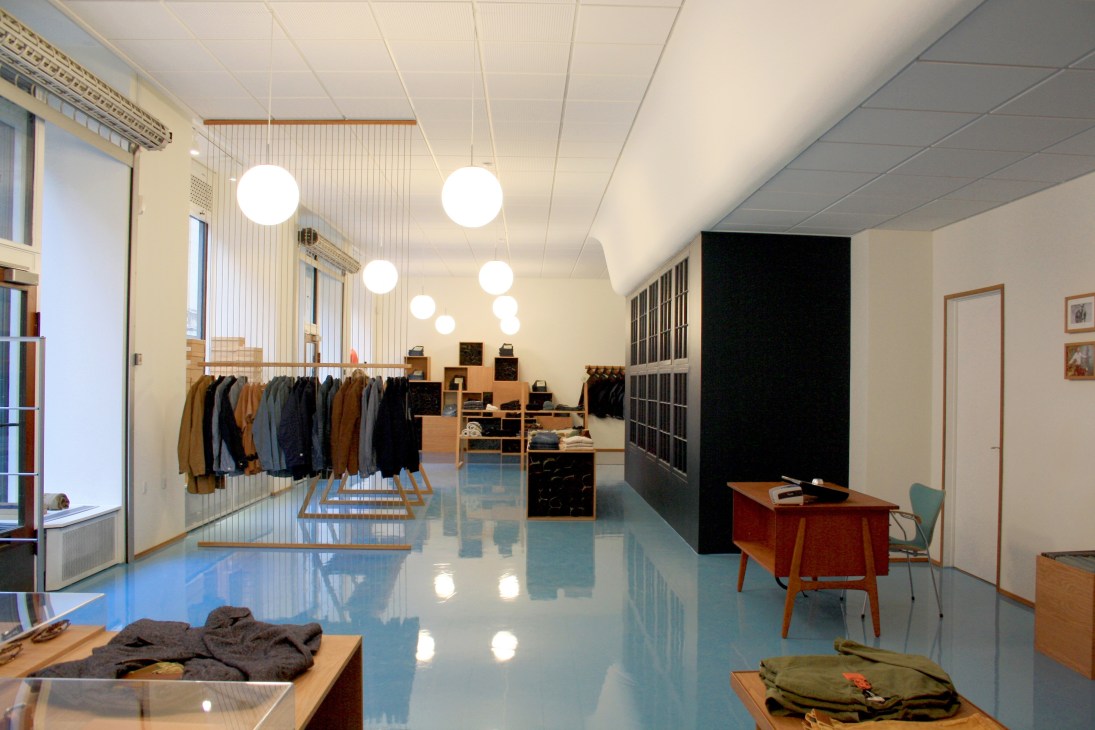Han Kjøbenhavn flagship store interior with minimalist design, pendant lighting, wooden furniture, and clothing displays.