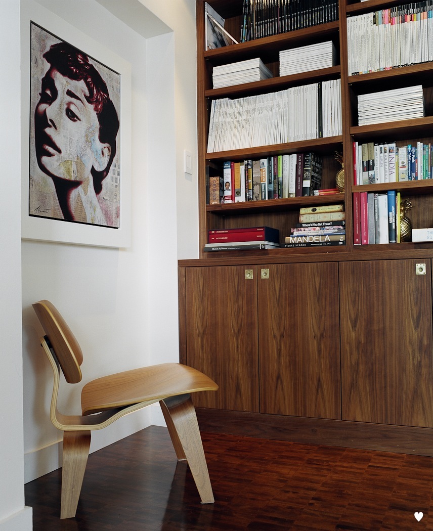 Modern wooden shelving unit displaying books with a pop art portrait and wooden chair.