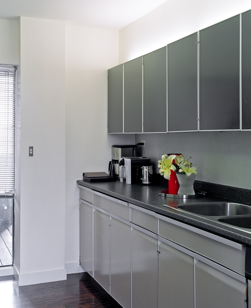 Modern kitchen with grey cabinetry, black countertop, stainless steel sink, and recessed lighting in a Habitat 67 unit.