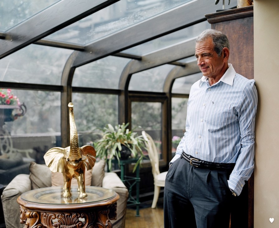 Frank Motter stands in an enclosed terrace with large windows overlooking the landscape.