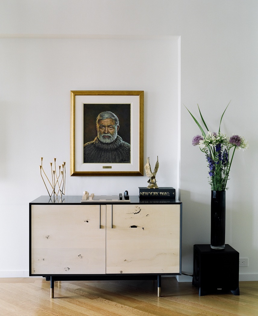 Modern living room with mid-century credenza, framed portrait, brass sculptural objects, and flowering vase.
