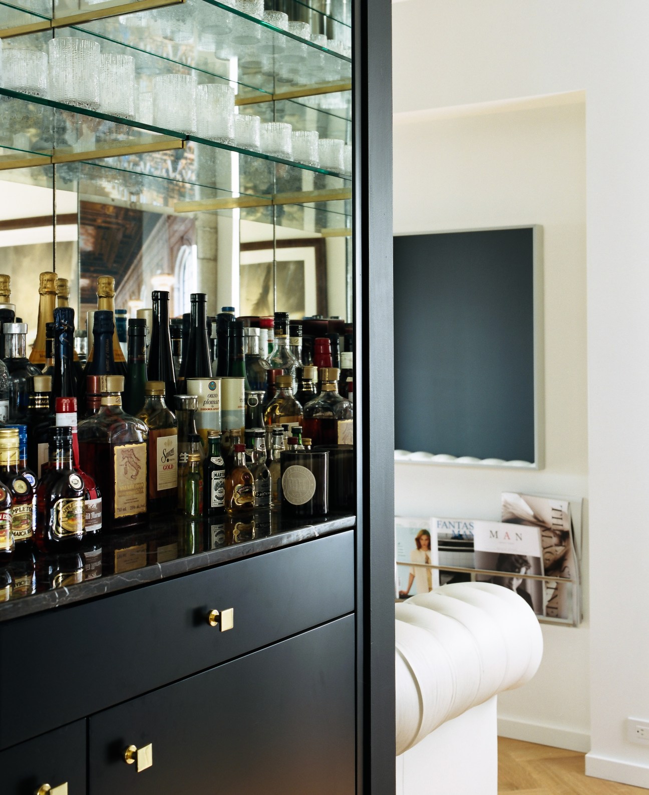 Glass-fronted bar cabinet with liquor bottles and brass fixtures in a modern apartment interior.