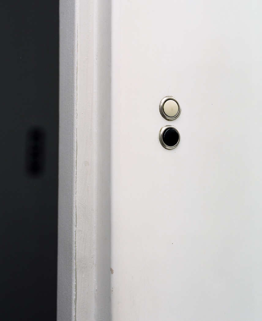 Two original low-voltage circular light switches mounted vertically on a white wall next to a dark vertical beam.