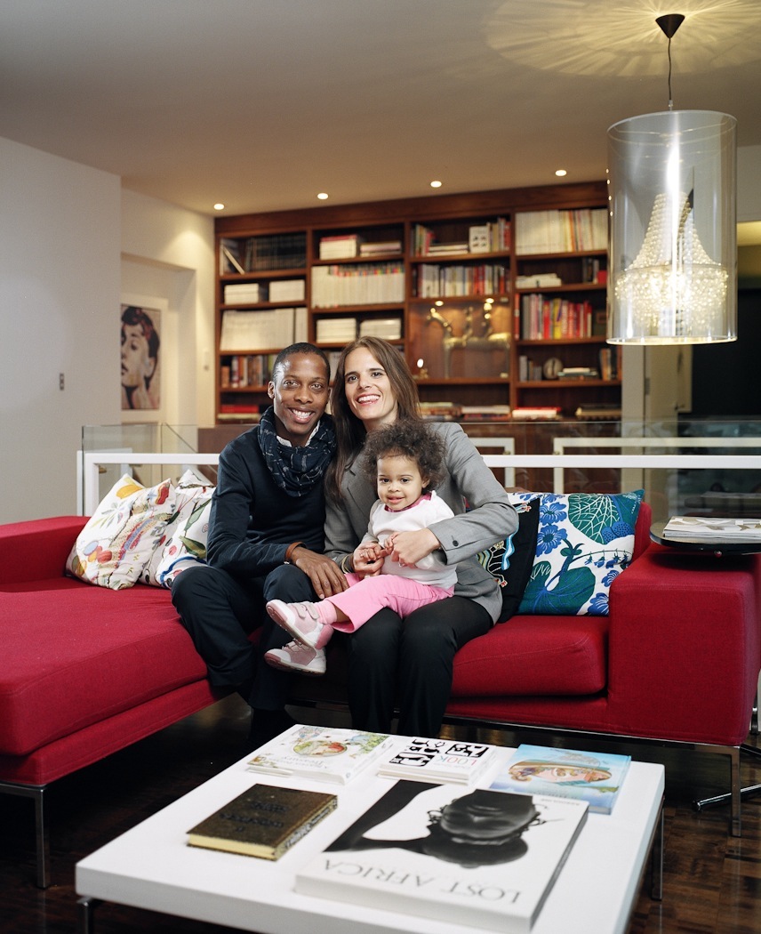 Dexter Peart, Maria Varvarikos-Peart and their daughter Kaya Sofia sit on a red sofa in their Habitat 67 living room.
