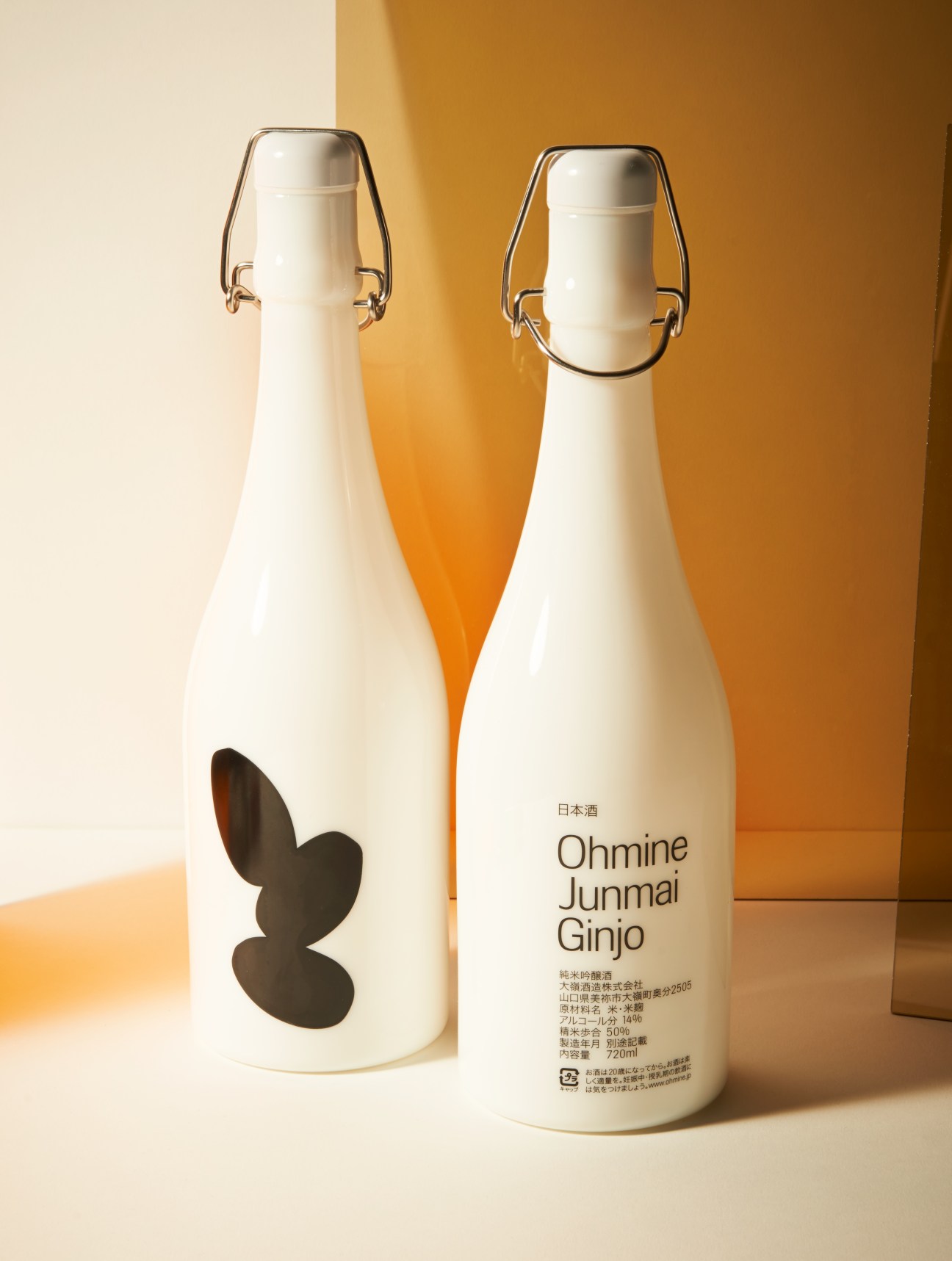 Two bottles of Ohmine Junmai Ginjo sake with white labels and metal clasps against a golden background.