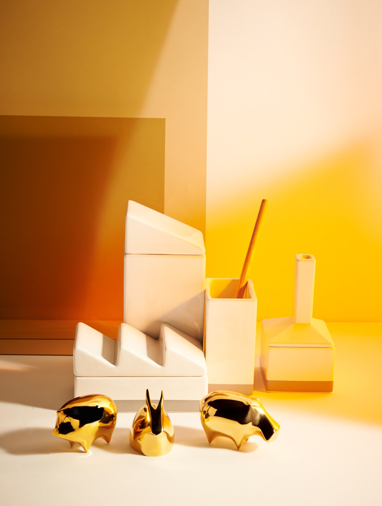 Porcelain desk organizers with brass animal figurines arranged against a yellow and orange geometric background.
