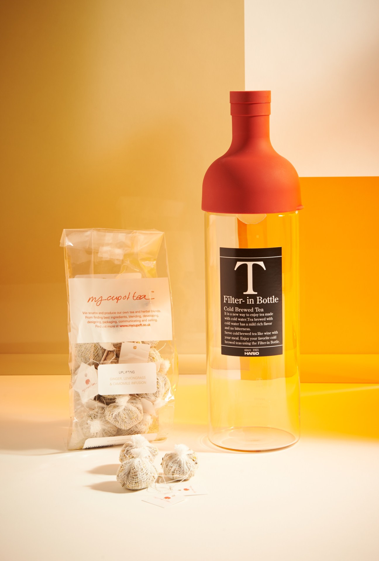 Hario cold-brew tea bottle with red cap next to My Cup of Tea teabags on warm-toned background.