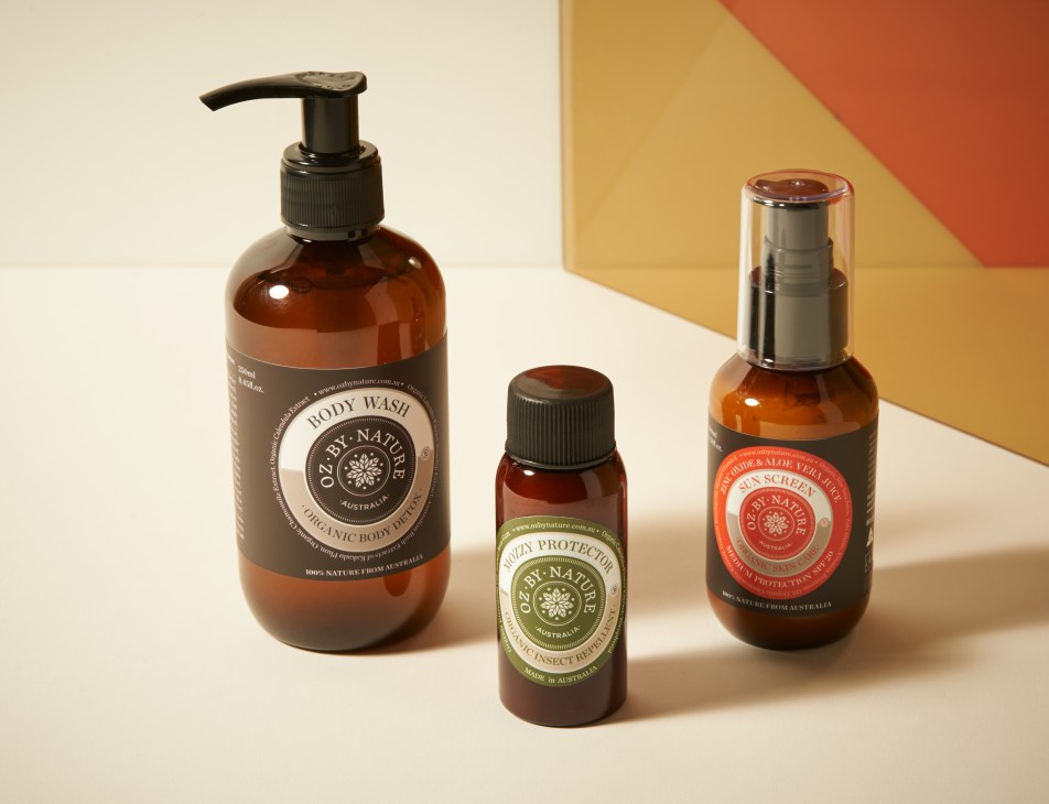 Three brown glass bottles of Oz by Nature organic skincare products displayed on a minimalist background.