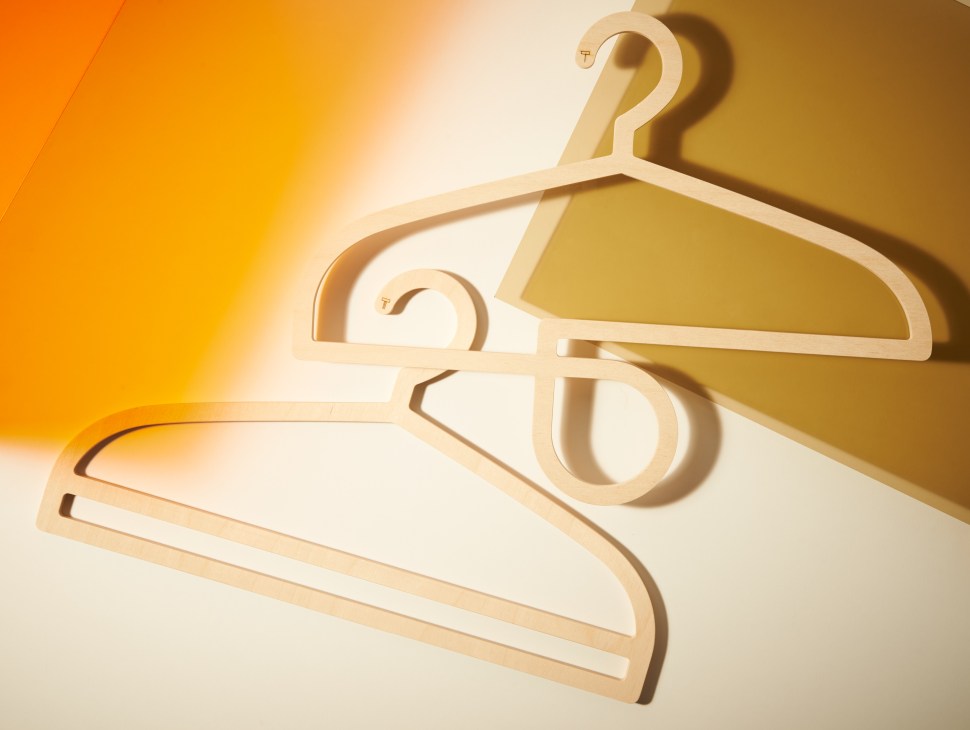 Toma wooden coat hangers in natural birch plywood arranged against a golden-yellow background.