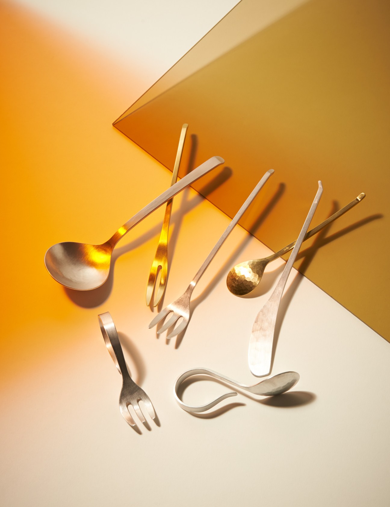Minimalist aluminium cutlery set by OEN shop designer Rieko Fujimoto displayed on a geometric gold and cream background.