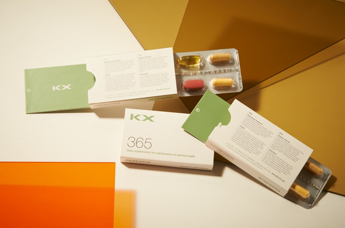 KX 365 daily supplements packaging with green branding and blister packs of vitamins displayed on a geometric background.