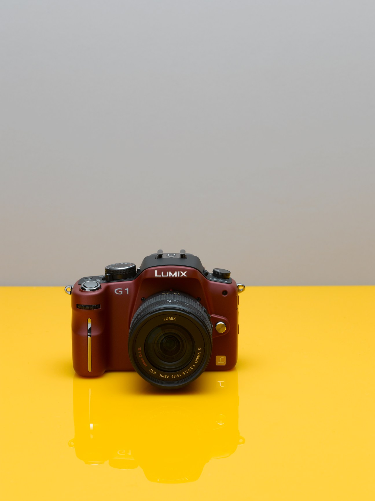 Red Panasonic Lumix DMC-G1 camera on yellow surface with grey background.