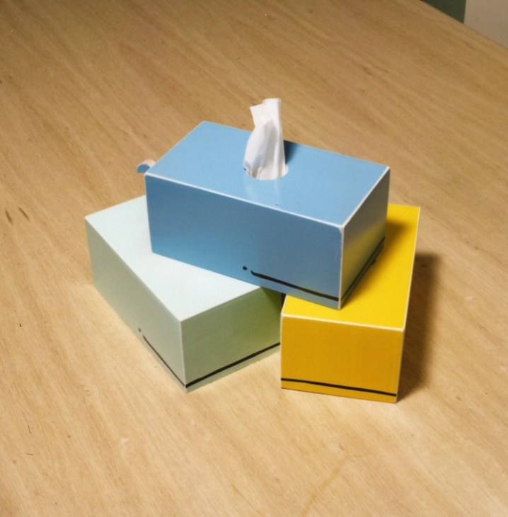 Stacked colorful tissue box holders in blue, white, and yellow on wooden surface.