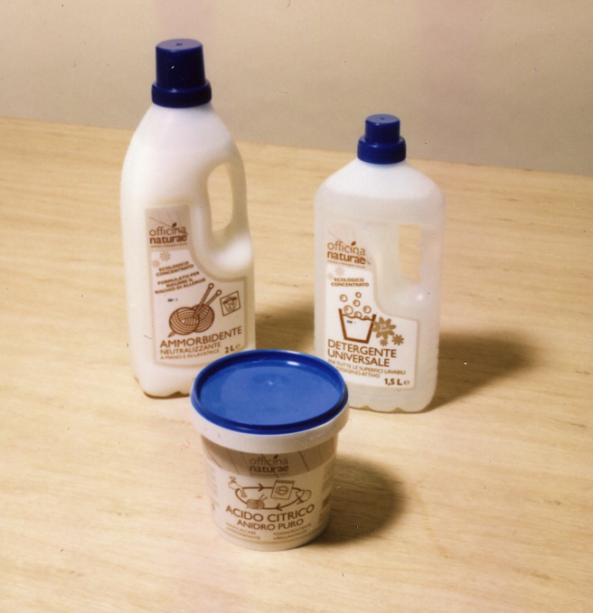Officina Naturae organic detergent bottles and container with blue caps on wooden surface.