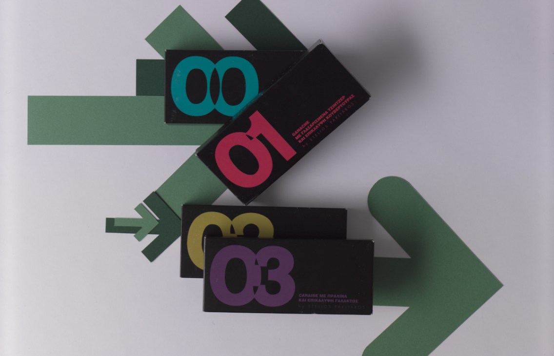 Stelios Parliaros chocolate bars with colored numbers and Greek text on black packaging arranged with green geometric shapes.