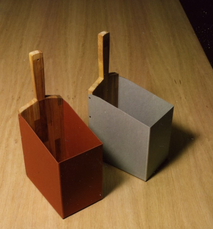 Two Postalco Handle Trashcans in brick red and black paperboard with natural wood handles on wooden surface.