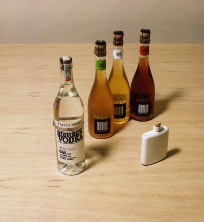 Bishkek vodka bottle, three Codice a Barre beer bottles, and white ceramic hip flask by Alexena Cayless on wooden surface.