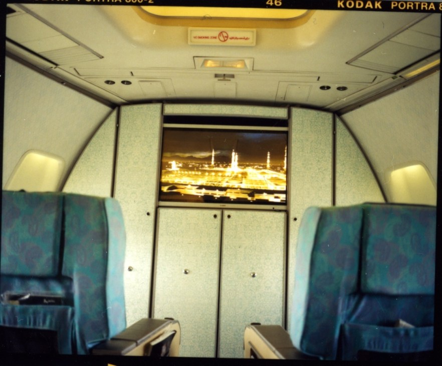 Airplane cabin interior showing illuminated display of Mecca on central screen during takeoff.