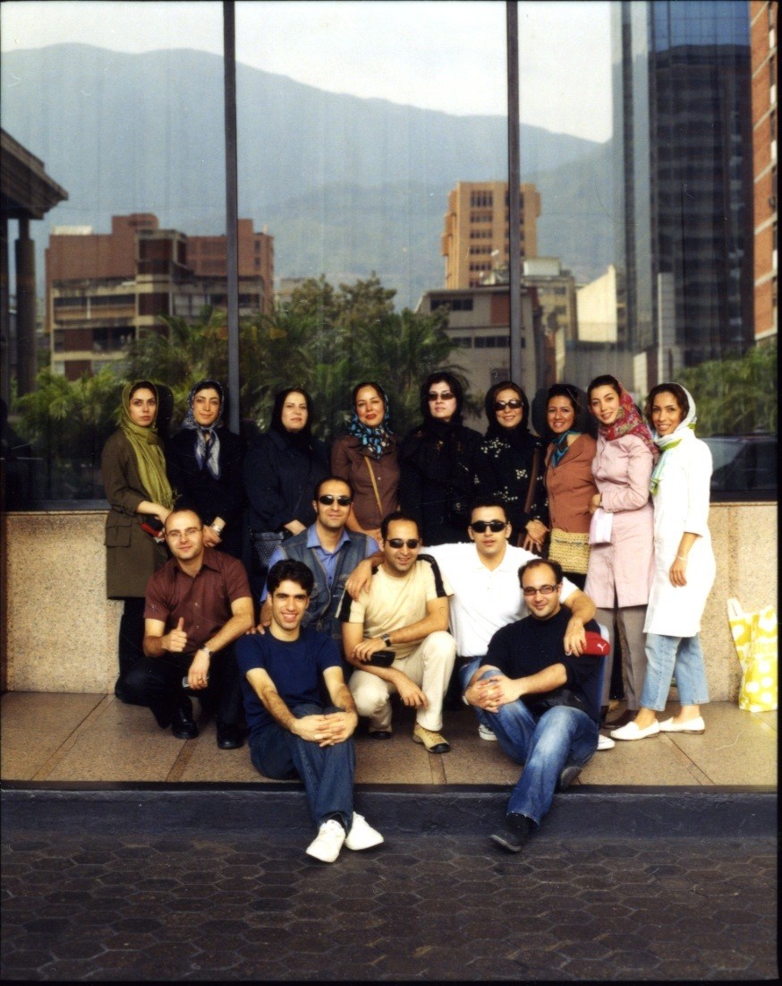 IranAir flight 744 crew posing together indoors with Tehran mountains and buildings visible through large windows behind them.
