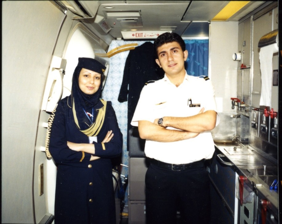 IranAir flight crew member in dark blue and gold uniform standing with male crew member in white shirt in aircraft galley