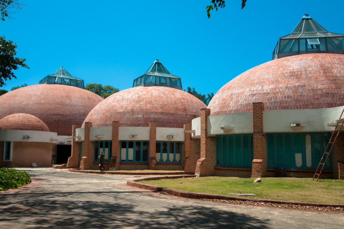 Modernist brick buildings with distinctive domed red-tiled roofs and glazed cupolas under clear blue sky.