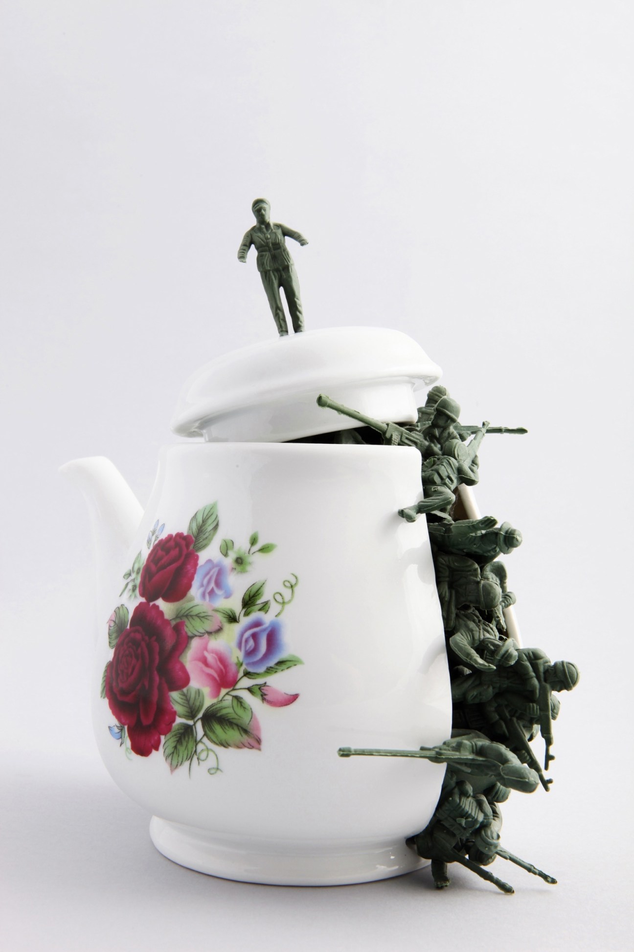White porcelain teapot with floral design and bronze figurative sculptures climbing its side.