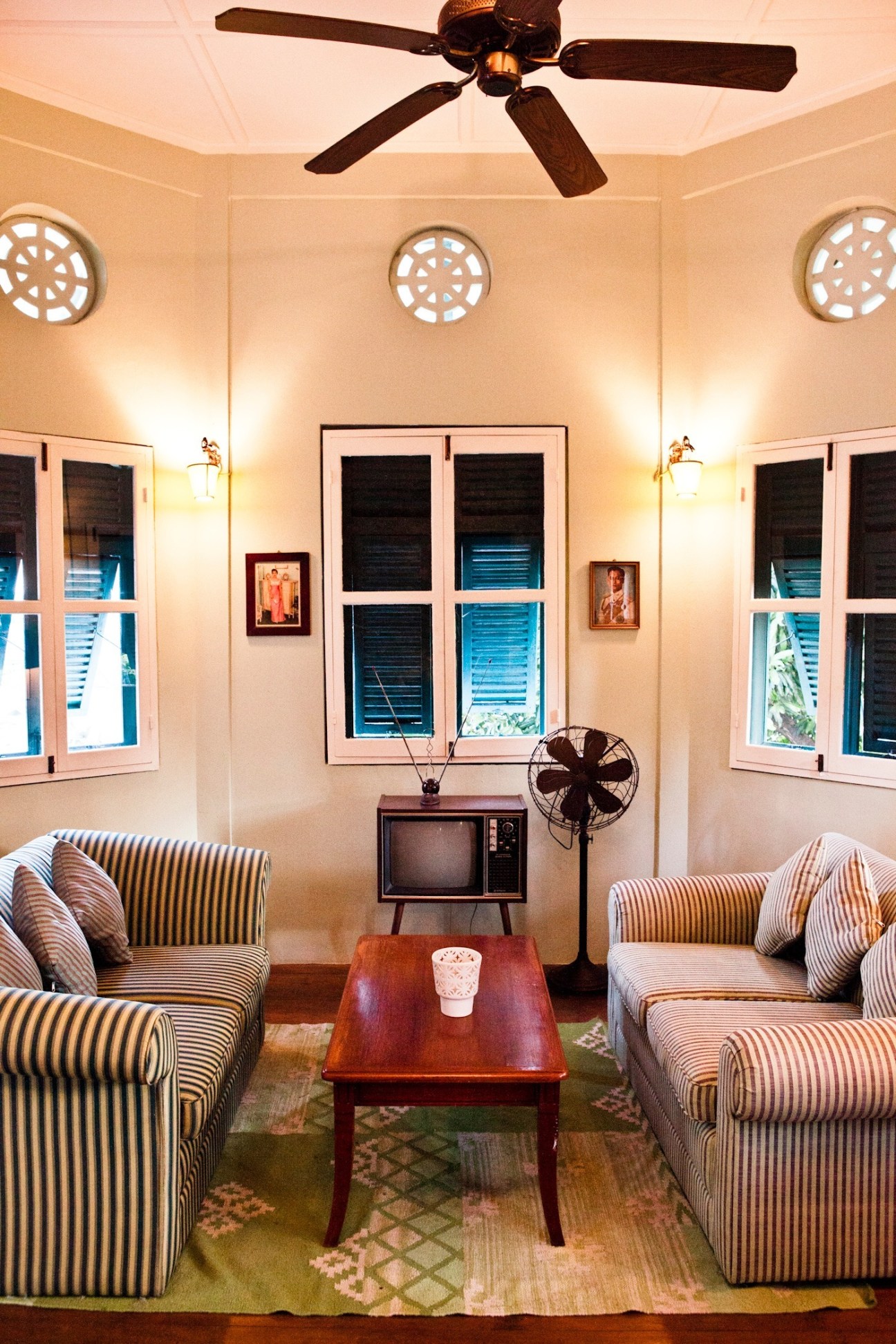 Upstairs lounge at Issaya Siamese Club with striped armchairs, vintage television, and decorative circular wall vents.