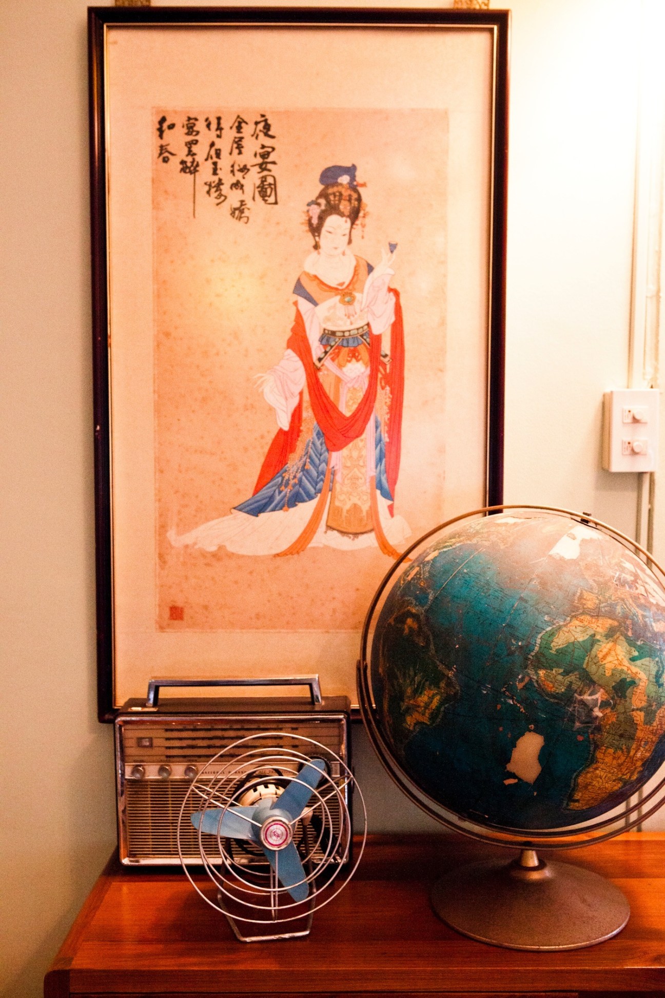 Vintage decorative items displayed in the Siamese Club upstairs lounge including a framed Asian artwork, globe, radio and fan.