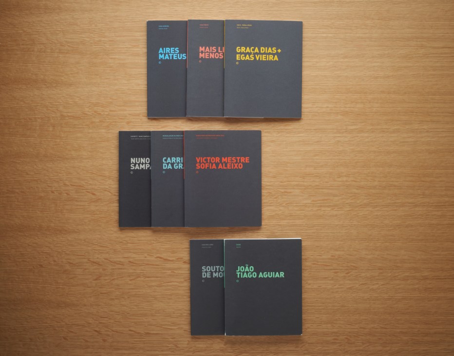 Eight dark-covered books with colorful text titles arranged on a wooden surface, featuring Portuguese architecture publications from Uzina Books.