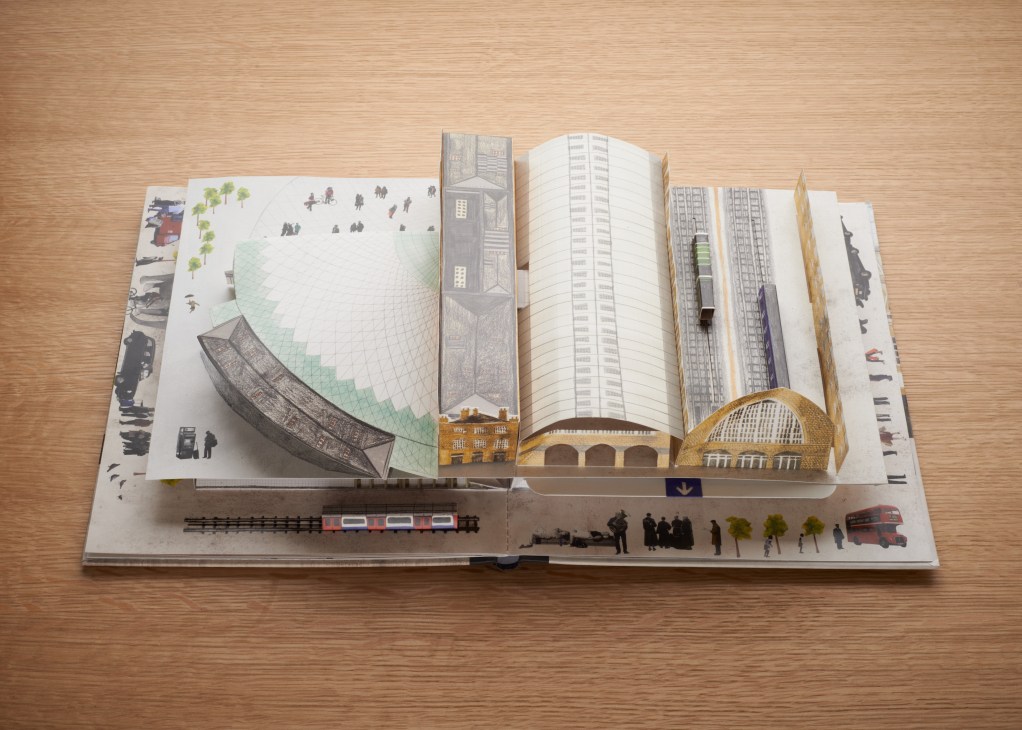 An open pop-up book depicting King's Cross station with detailed 3D architectural elements and miniature figures on a wooden surface.