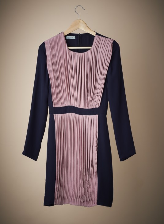 Navy and pink pleated dress on wooden hanger against neutral background.