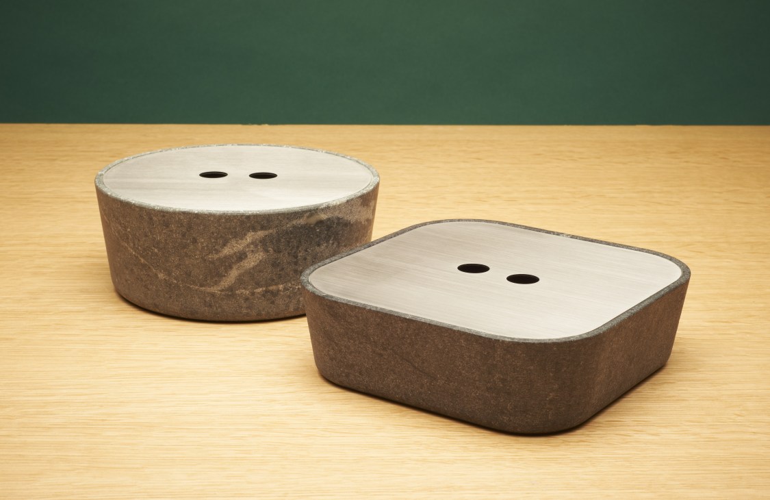 Two soapstone serving dishes by Strato in round and rectangular shapes with light-colored lids featuring two holes each.