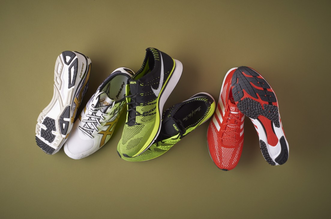 Three running shoes displayed on a tan background: white and gold Asics, neon yellow and black Nike, and red and white shoe with black accents.