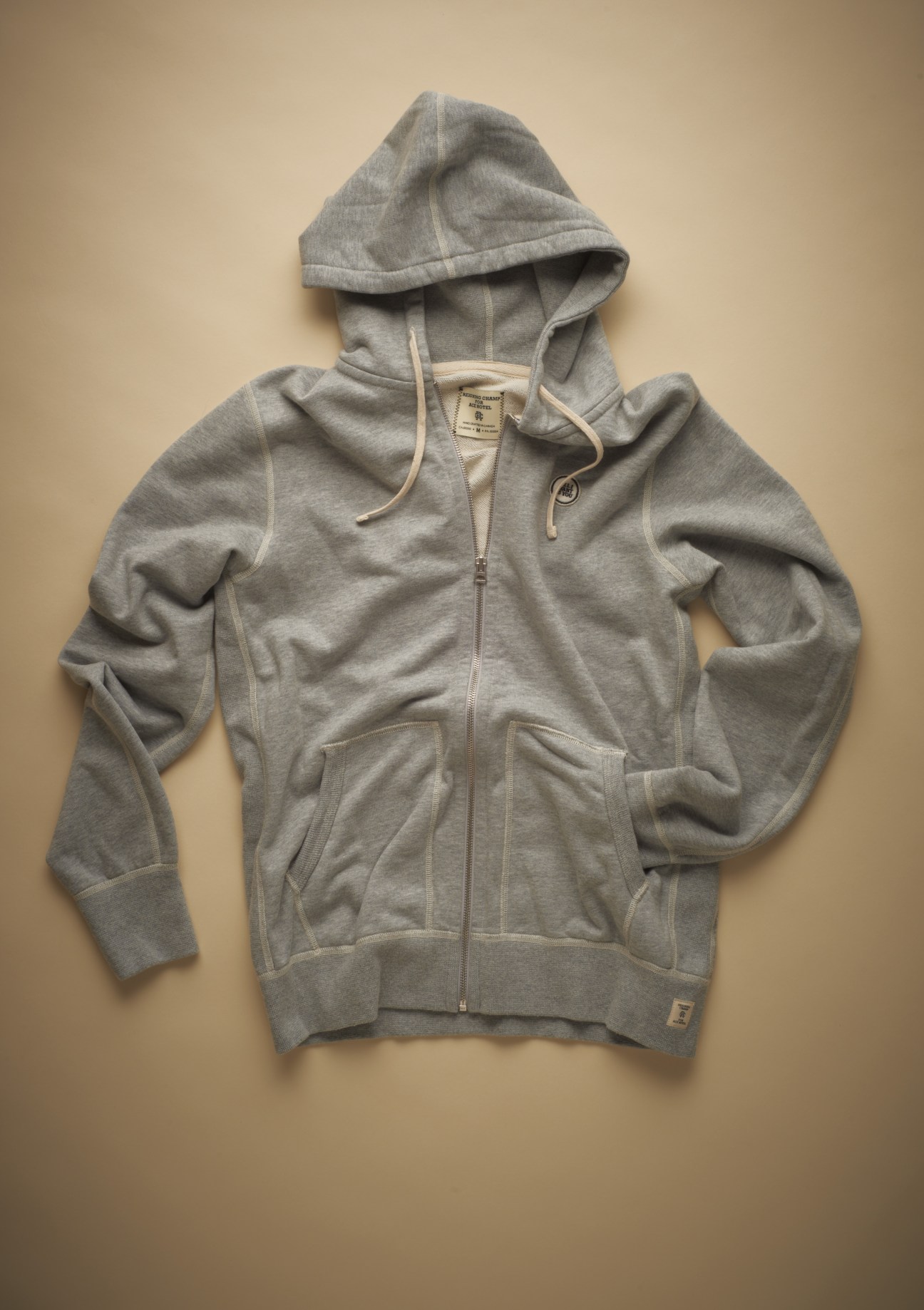 Ace x Reigning Champ gray zip-up hoodie with drawstring displayed flat on beige background.
