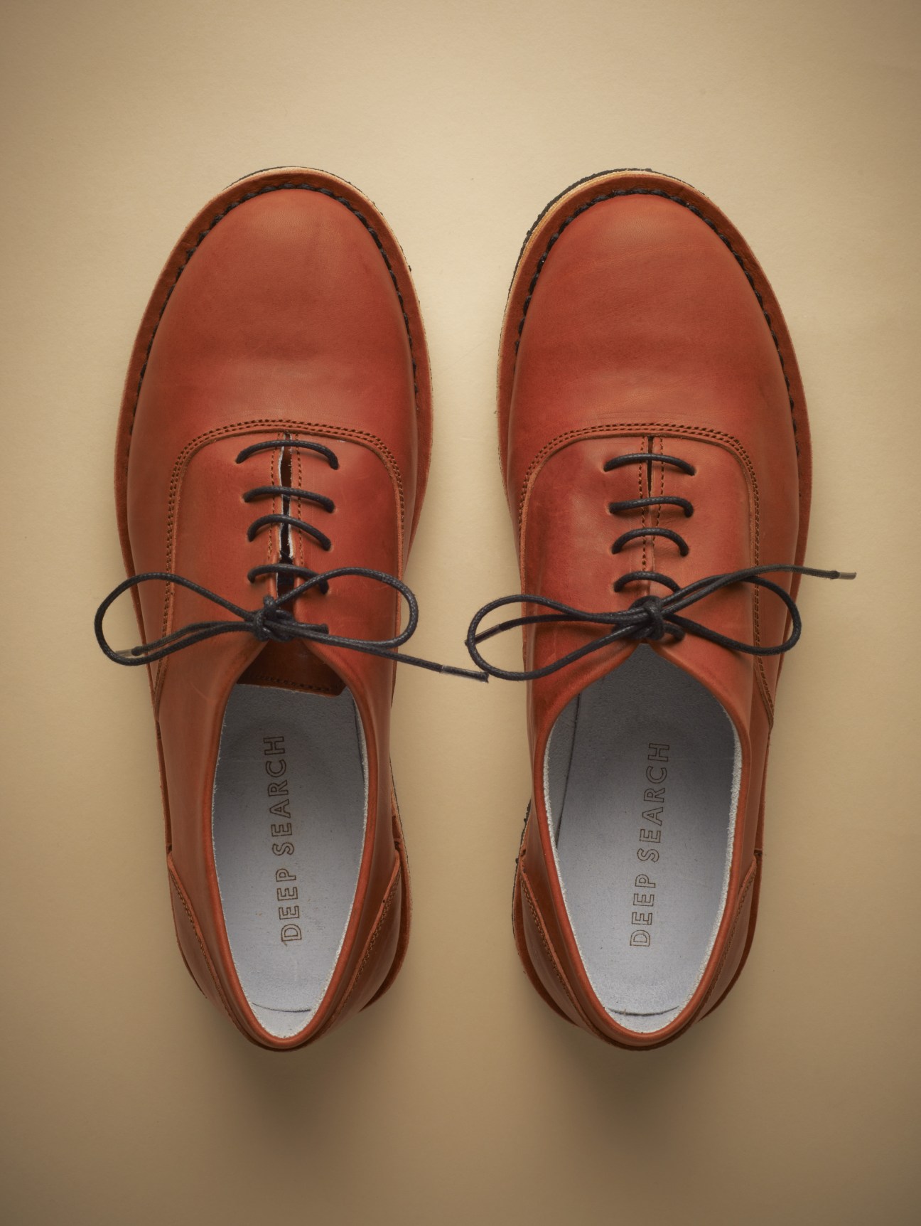 Pair of Deep Search handcrafted leather oxfords in rust-brown with black laces, displayed flat on a neutral background.