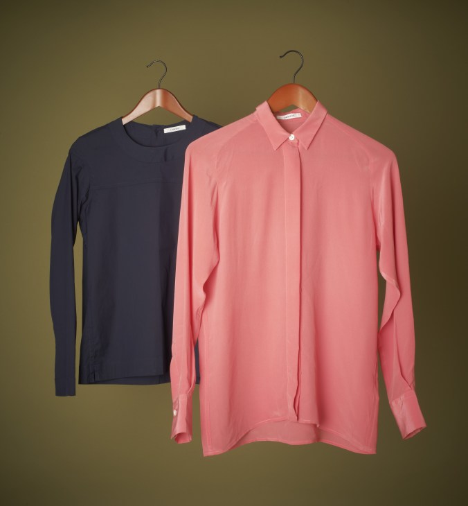Two Lareida women's shirts on wooden hangers against a mustard background: a navy long-sleeved shirt and a coral pink button-up shirt.