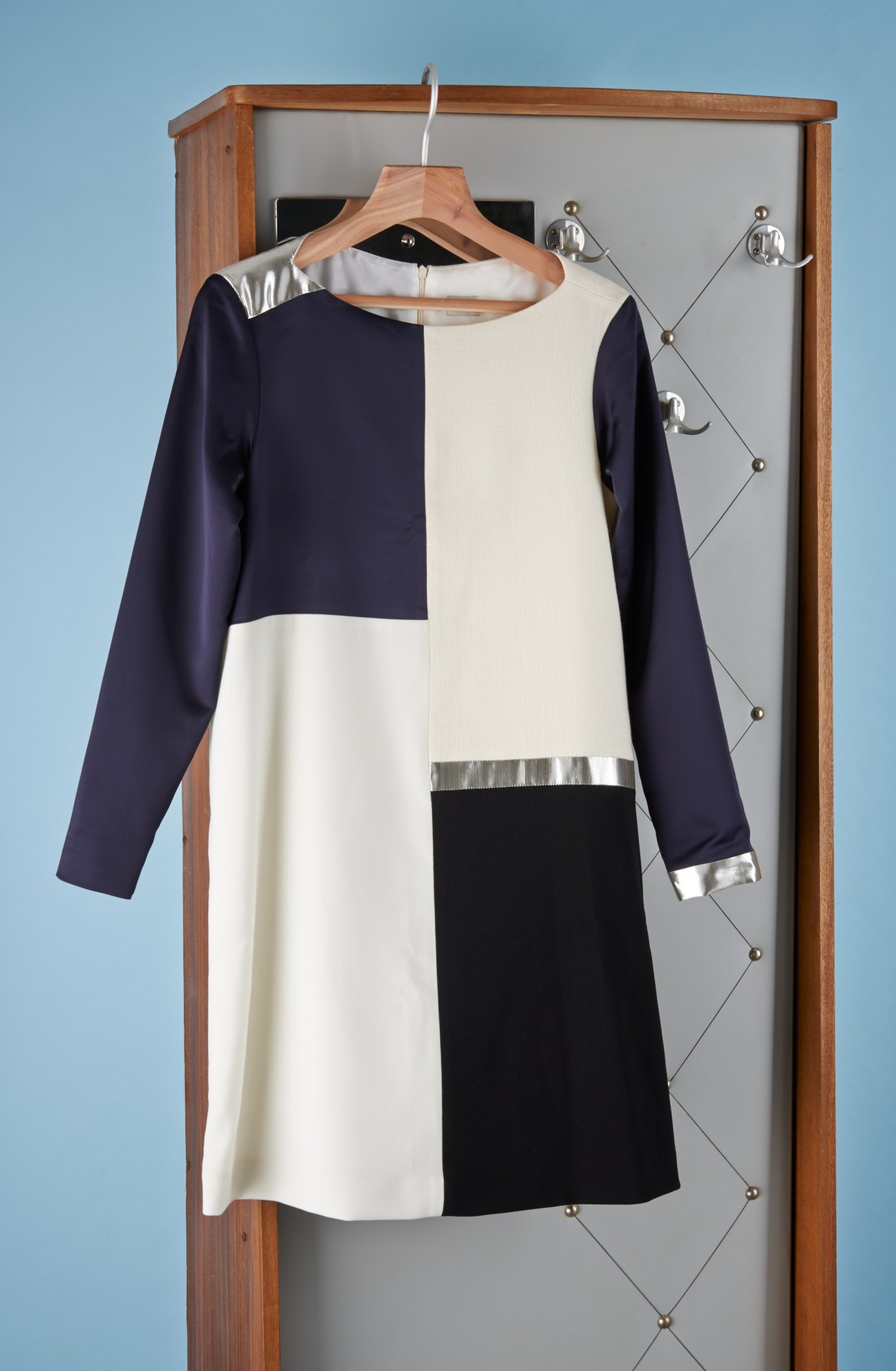 Liebig panel Anouk dress in navy, cream and black with silver metallic trim on wooden hanger against blue background.