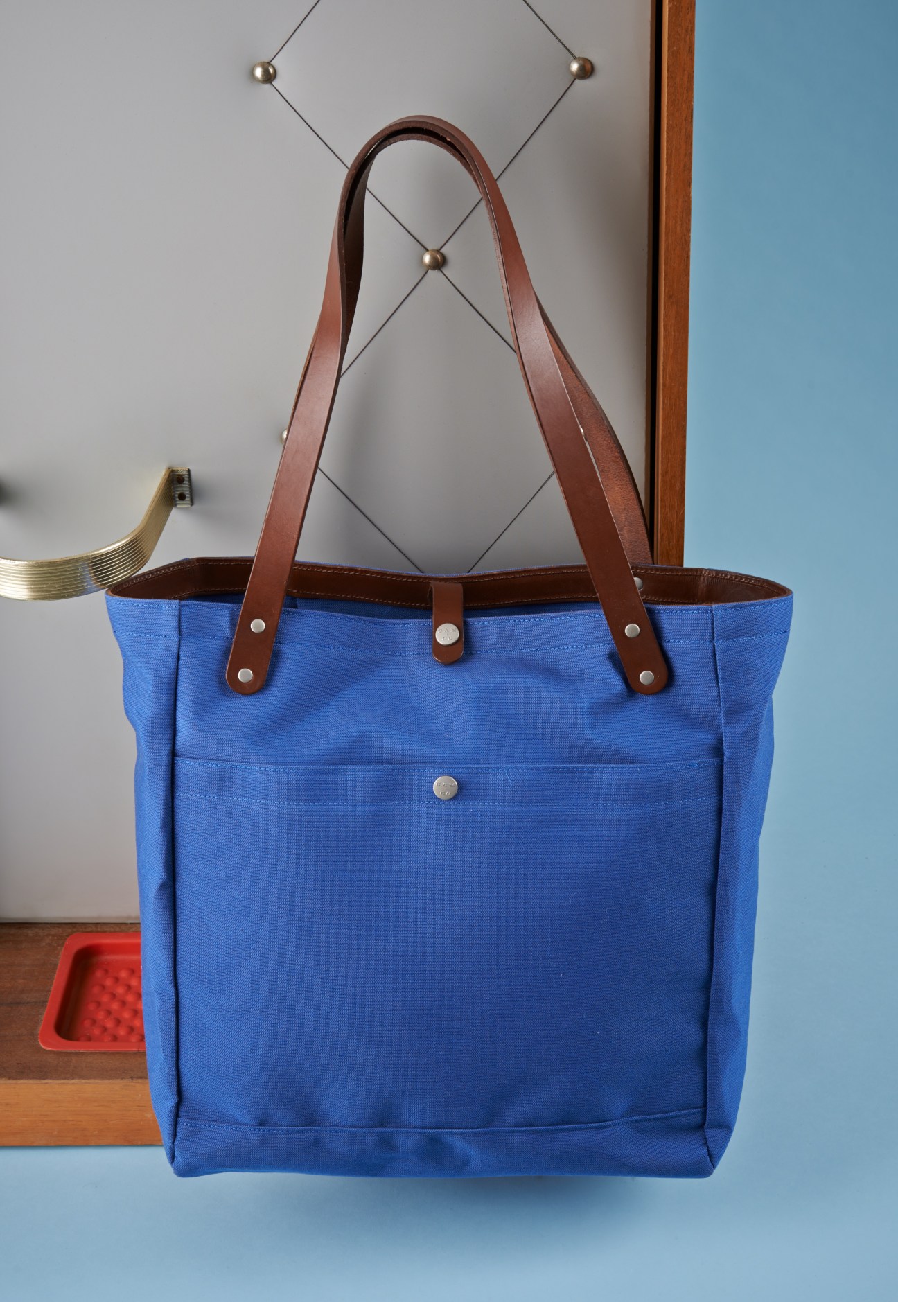 Blue canvas tote bag with brown leather handles and trim hanging on white display rack.