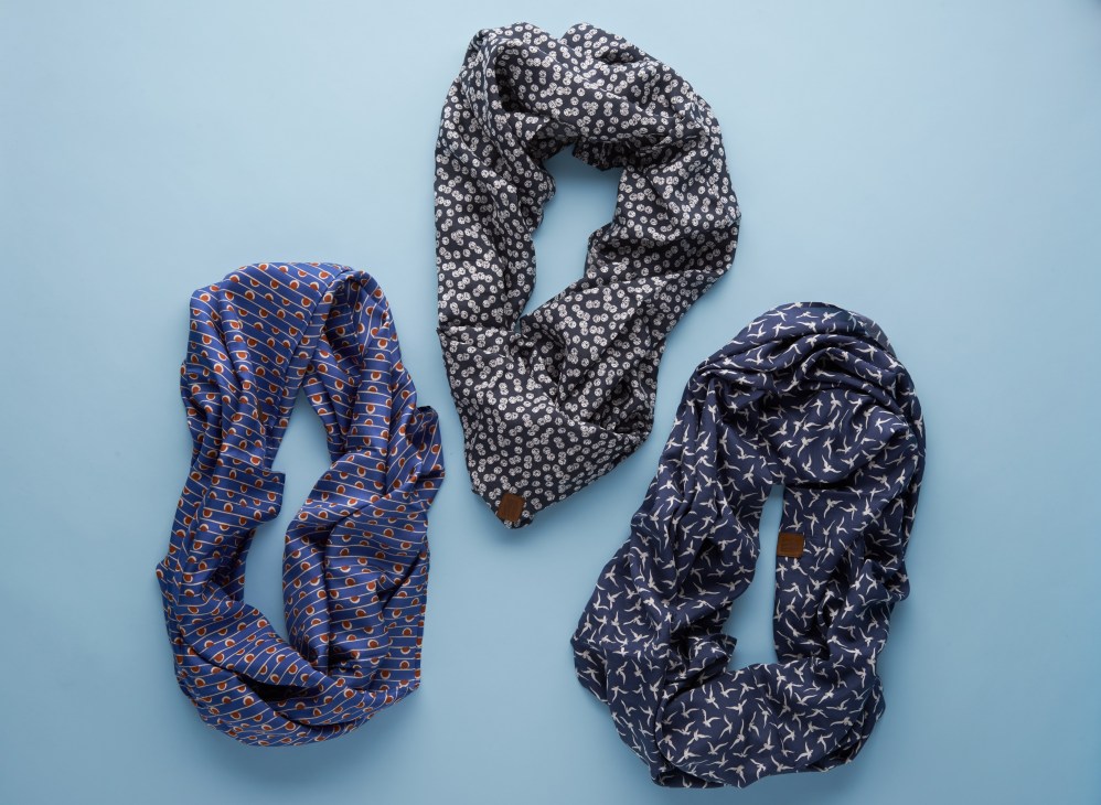 Three patterned scarves arranged on a light blue background, including a blue scarf with geometric patterns and two navy scarves with different prints.