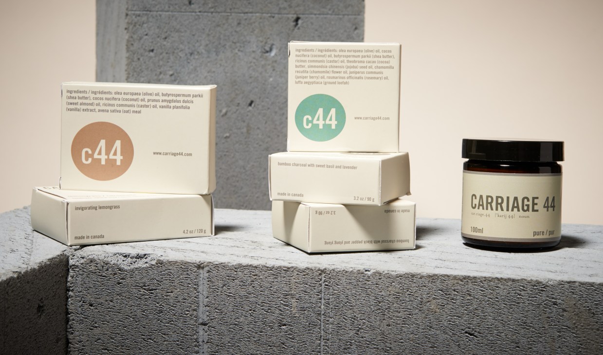 Carriage 44 handmade soaps displayed in cream-colored boxes with c44 logo and glass jar on concrete surface.