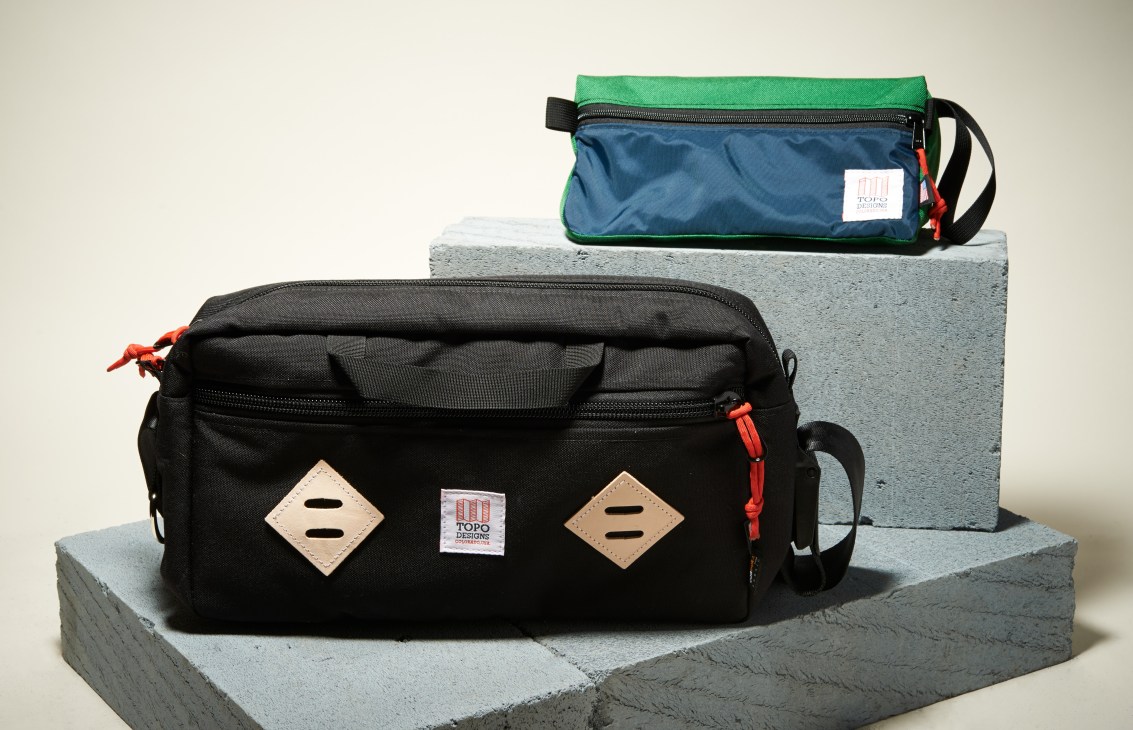 Topo Designs colorful bags displayed on concrete blocks, including black and green styles with leather accents.