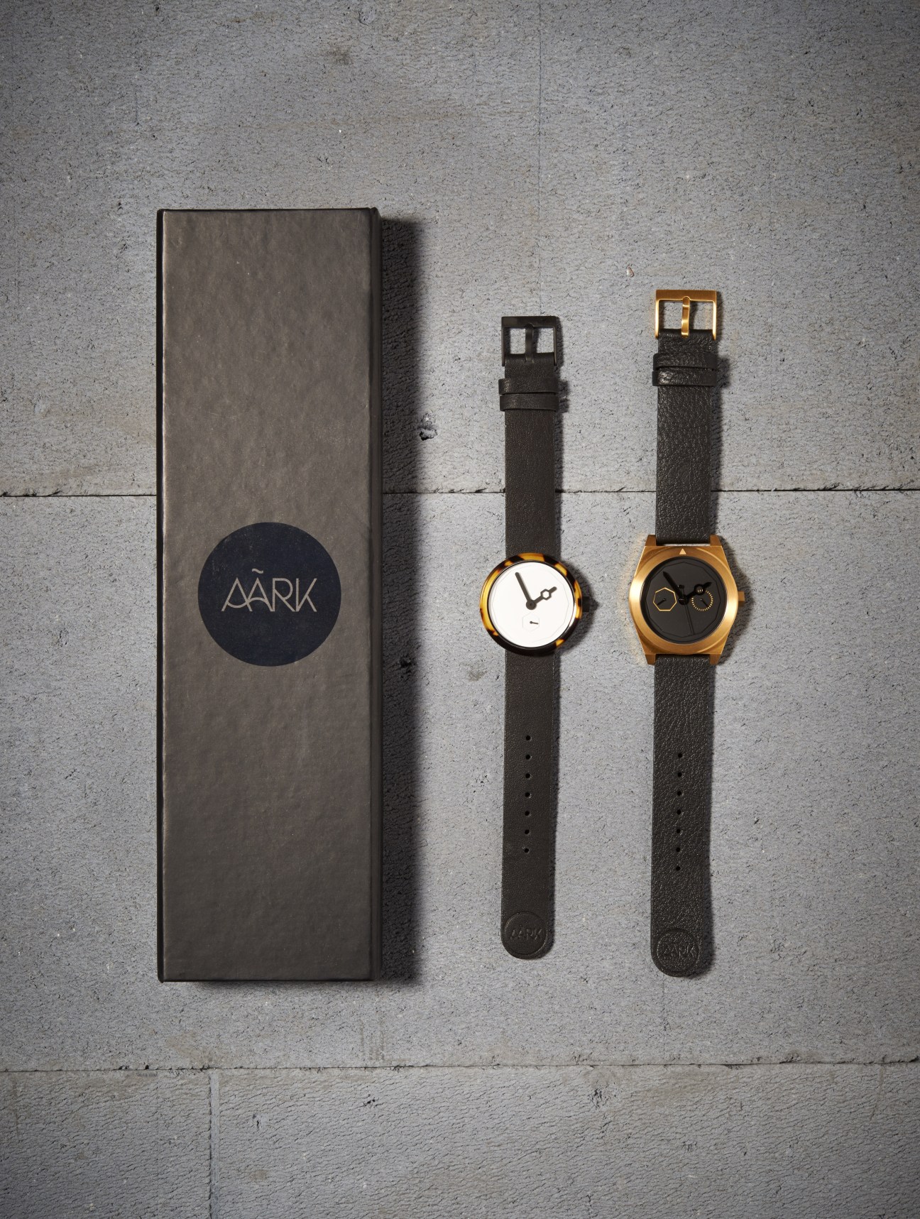 AÃRK Collective watches displayed with packaging box, showing minimalist design with leather straps and metal cases.