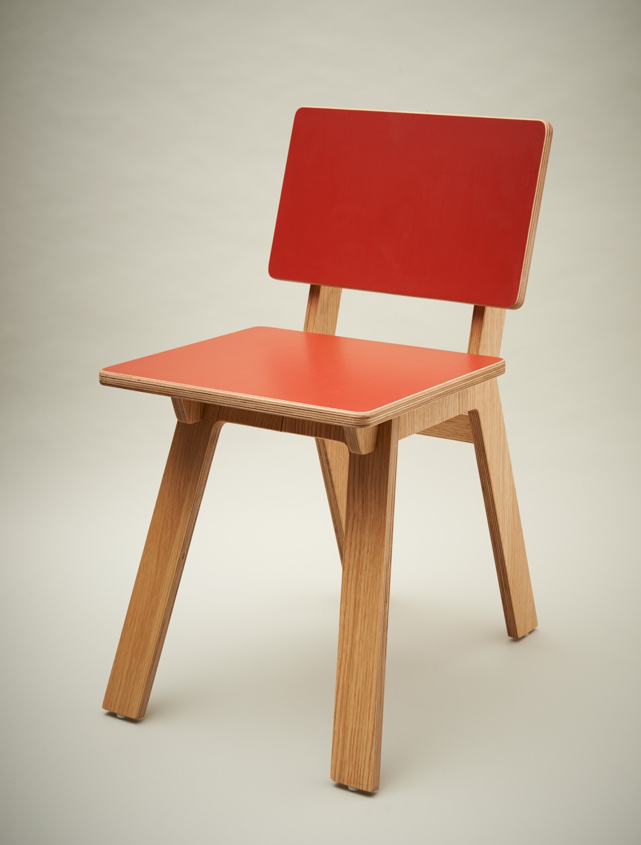 Red and natural wood chair with angled legs and rectangular backrest against neutral background.