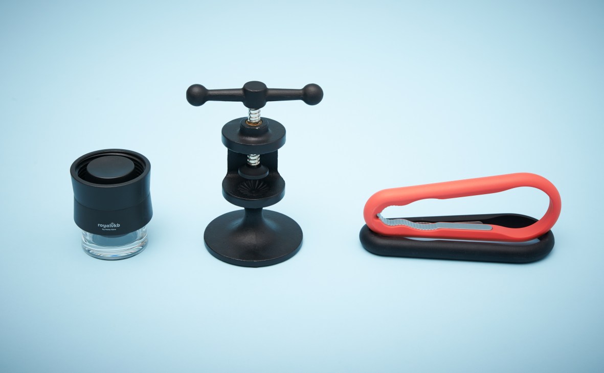 Three modern nutcrackers displayed against a light blue background: a black Royal VKB compact model, a black cast iron Hobart nutcracker, and a red and black silicone Normann Copenhagen design.
