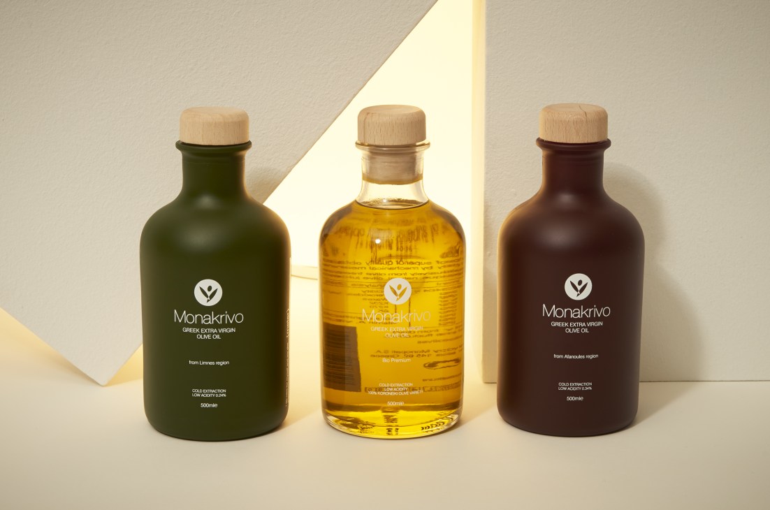 Three bottles of Monakrivo Greek extra virgin olive oil in different color varieties with wooden caps.