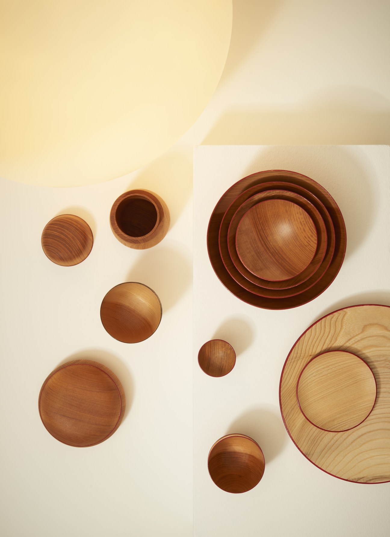 Overhead view of Kazushige Miyake wooden tableware in various sizes arranged on white background.