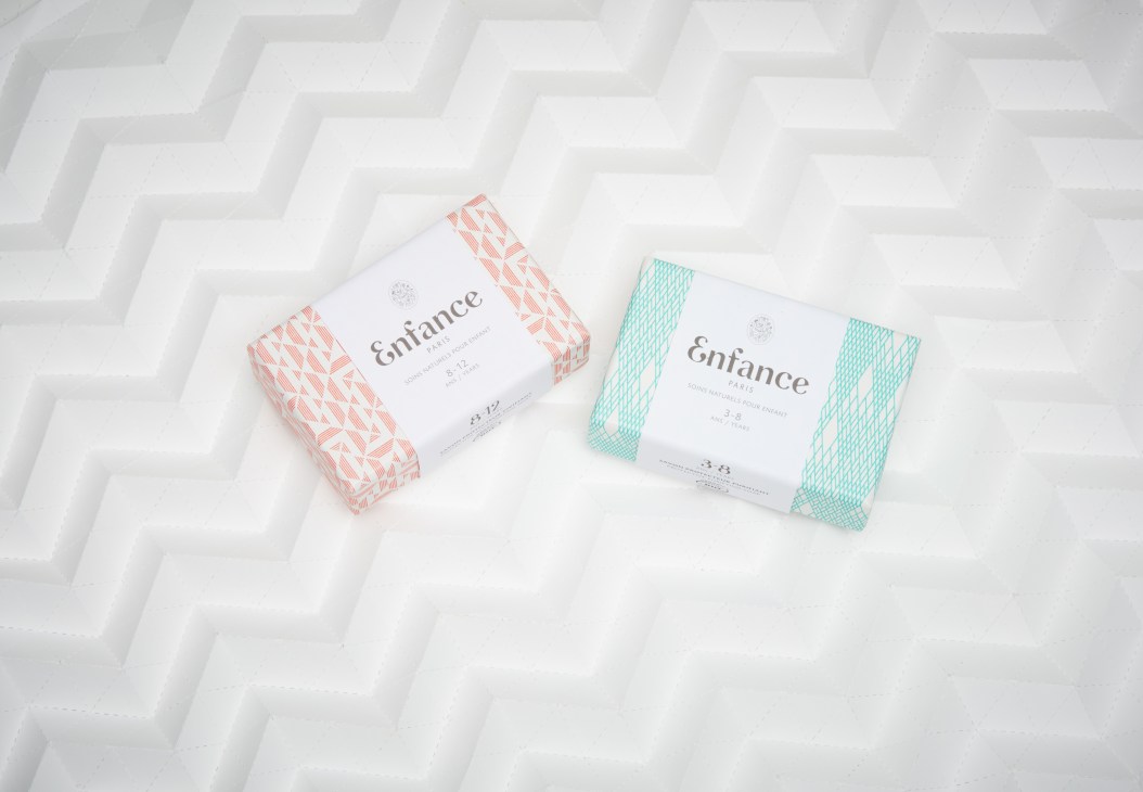 Two Enfance Paris children's soap boxes with patterned wrappers in coral and turquoise on a white textured background.