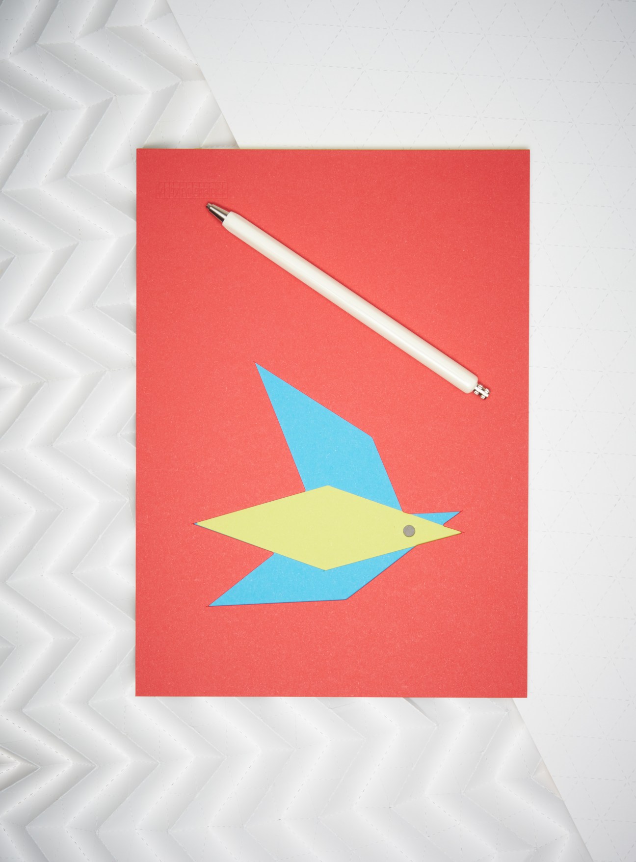 White pen and colorful geometric fish illustration on red paper.