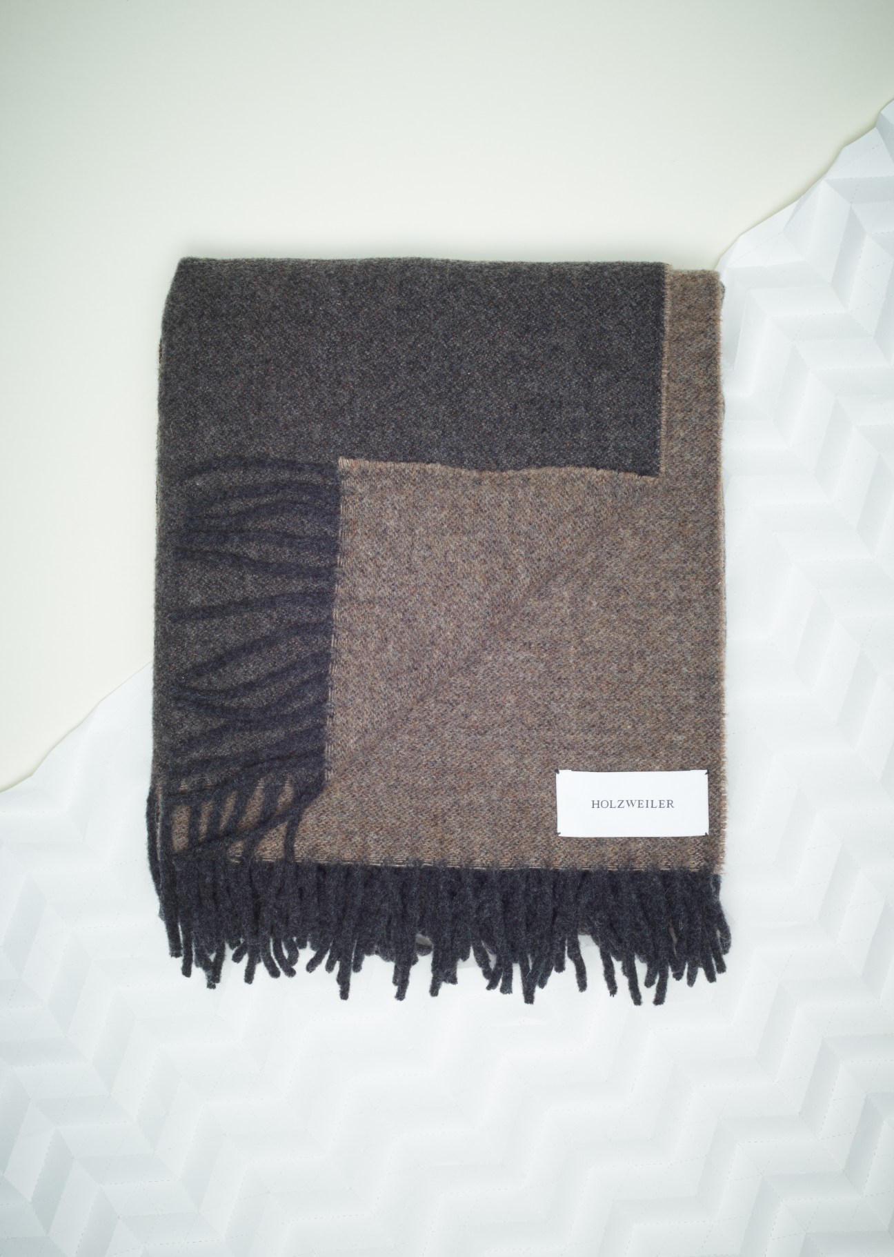 Holzweiler wool-cashmere scarf in charcoal and taupe with fringe, displayed flat on white fabric.