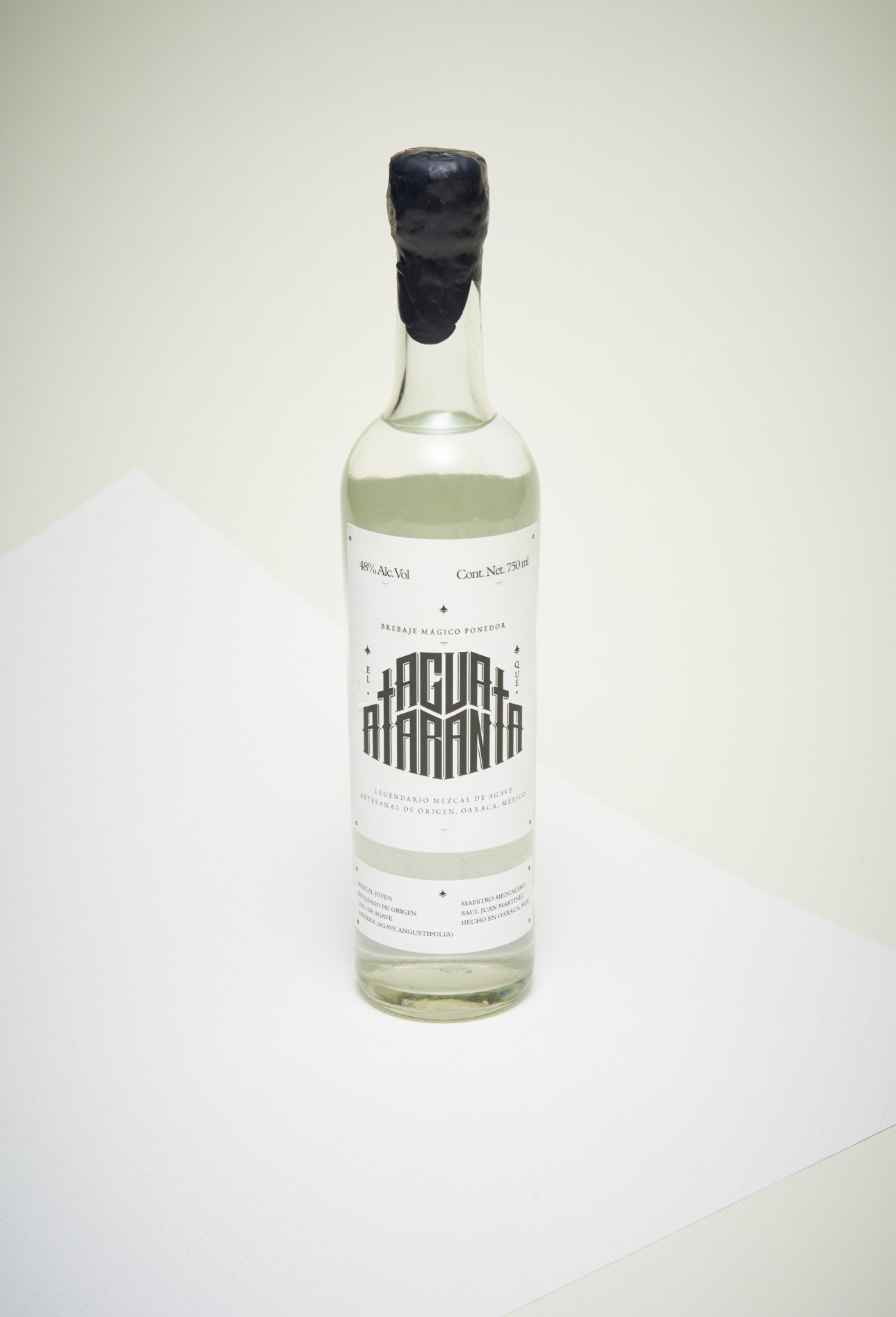Agua Que Ataranta mezcal bottle with pale green liquid and black wax seal against white background.
